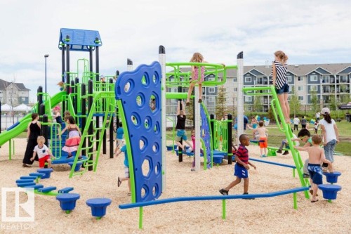 The property features a recreational playground area with various blue and green climbing structures and slides, set on a wood chip surface - 14 1140 Chappelle Boulevard, Edmonton, AB - Outdoor