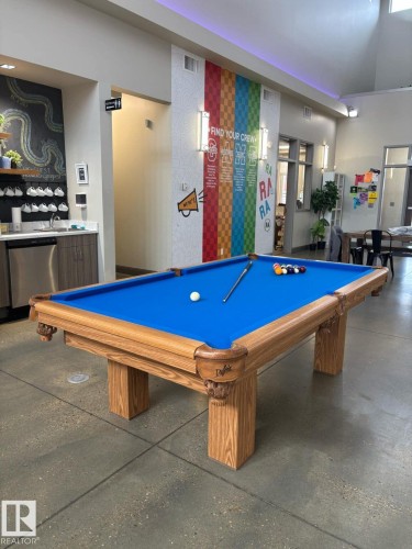 Recreation area featuring a billiard table with a wooden frame and blue felt, concrete flooring, and a refreshment station with a stainless steel dishwasher - 14 1140 Chappelle Boulevard, Edmonton, AB - Indoor Photo Showing Other Room