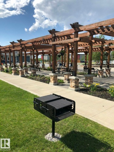 The property features a large grassy area with a charcoal grill, a concrete pathway, and a wooden pergola with stone pillars - 14 1140 Chappelle Boulevard, Edmonton, AB - Outdoor
