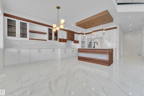 Dual tone kitchen featuring a kitchen island with sink, a chandelier, glass insert cabinets, two tone cabinets, and open shelves - 231 Crystal Creek Drive, Leduc, AB - Indoor