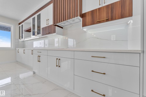 Kitchen with glass insert cabinets, two tone color scheme, light marble finish flooring, and light stone counters - 231 Crystal Creek Drive, Leduc, AB - Indoor