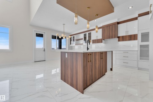 Dual tone kitchen with dual tone cabinetry, light marble finish floors, glass fronted cabinets, a kitchen island with sink, and modern cabinets - 231 Crystal Creek Drive, Leduc, AB - Indoor Photo Showing Kitchen
