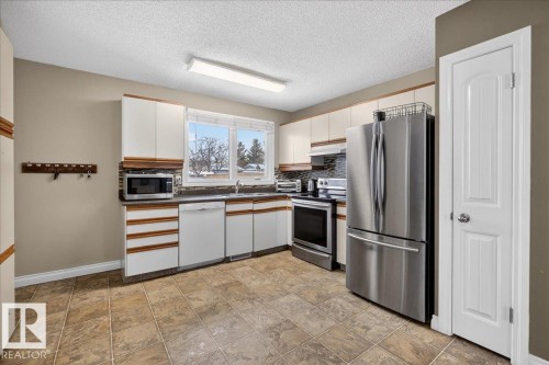 Kitchen featuring stainless steel appliances, decorative backsplash, dual tone cabinets, a textured ceiling, and dark countertops - 8804 38 Avenue, Edmonton, AB - Indoor Photo Showing Kitchen With Double Sink