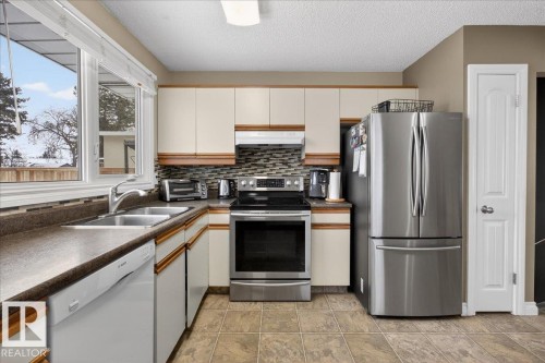 Two tone kitchen featuring stainless steel appliances, dark countertops, a textured ceiling, backsplash, and dual tone cabinets - 8804 38 Avenue, Edmonton, AB - Indoor Photo Showing Kitchen With Double Sink