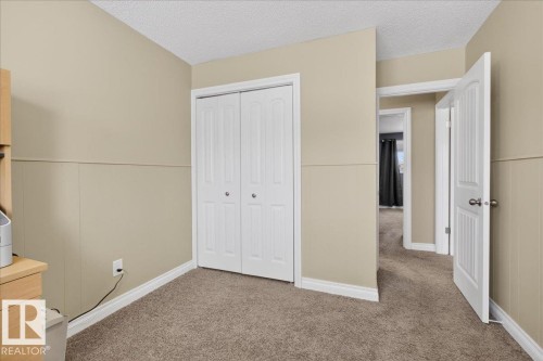 Unfurnished bedroom with light carpet, a closet, a textured ceiling, and wainscoting - 8804 38 Avenue, Edmonton, AB - Indoor