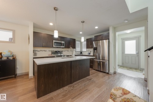 Kitchen featuring stainless steel appliances, pendant lighting, dark wood finish cabinetry, an island with sink, and light wood-type flooring - 17528 58 Street, Edmonton, AB - Indoor Photo Showing Kitchen With Stainless Steel Kitchen With Upgraded Kitchen