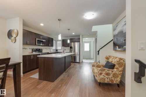 Kitchen featuring stainless steel appliances, light wood-type flooring, an island with sink, hanging light fixtures, and dark wood finish cabinetry - 17528 58 Street, Edmonton, AB - Indoor Photo Showing Kitchen With Upgraded Kitchen
