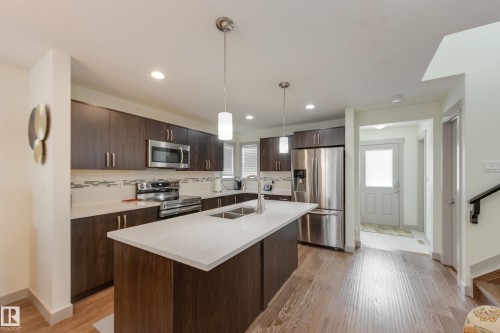 Kitchen with stainless steel appliances, decorative light fixtures, dark wood finish cabinets, and light wood-style floors - 17528 58 Street, Edmonton, AB - Indoor Photo Showing Kitchen With Stainless Steel Kitchen With Double Sink With Upgraded Kitchen
