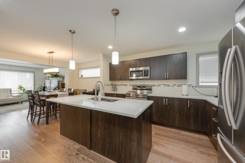 Kitchen featuring stainless steel appliances, dark wood finish cabinets, a kitchen island with sink, decorative light fixtures, and tasteful backsplash - 17528 58 Street, Edmonton, AB - Indoor Photo Showing Kitchen With Stainless Steel Kitchen With Double Sink With Upgraded Kitchen