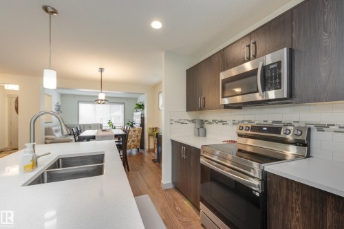 Kitchen featuring stainless steel appliances, dark wood finish cabinetry, and light wood finished floors - 17528 58 Street, Edmonton, AB - Indoor Photo Showing Kitchen With Stainless Steel Kitchen With Double Sink With Upgraded Kitchen