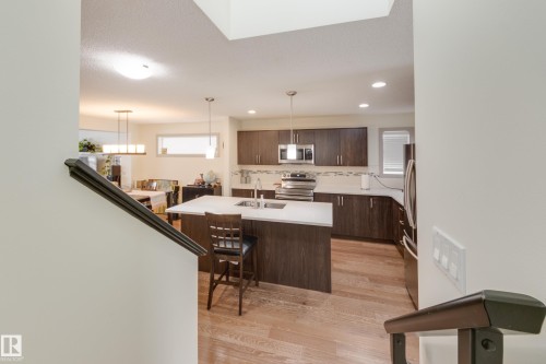 Kitchen featuring light wood-type flooring, stainless steel appliances, hanging light fixtures, dark wood finish cabinets, and a kitchen breakfast bar - 17528 58 Street, Edmonton, AB - Indoor Photo Showing Kitchen With Upgraded Kitchen
