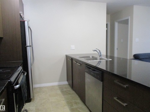 Kitchen with a peninsula, stainless steel appliances, dark stone countertops, dark wood finish cabinetry, and modern cabinets - 3309 9351 Simpson Drive, Edmonton, AB - Indoor Photo Showing Kitchen With Double Sink