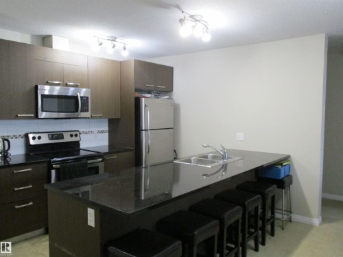 Kitchen with stainless steel appliances, a kitchen breakfast bar, a peninsula, tasteful backsplash, and modern cabinets - 3309 9351 Simpson Drive, Edmonton, AB - Indoor Photo Showing Kitchen With Double Sink