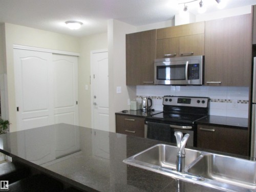 Kitchen with stainless steel appliances, a kitchen breakfast bar, dark stone countertops, and backsplash - 3309 9351 Simpson Drive, Edmonton, AB - Indoor Photo Showing Kitchen With Double Sink