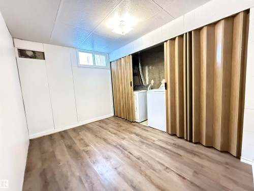 Below grade area with light wood-style floors, washer and dryer, and a drop ceiling - 9034 60 Street, Edmonton, AB - Indoor Photo Showing Other Room