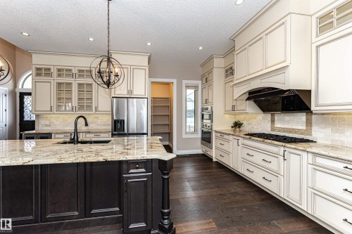 Kitchen with glass fronted cabinets, light stone counters, stainless steel appliances, dark wood-style floors, and backsplash - 3520 Watson Point(E), Edmonton, AB - Indoor Photo Showing Kitchen With Upgraded Kitchen