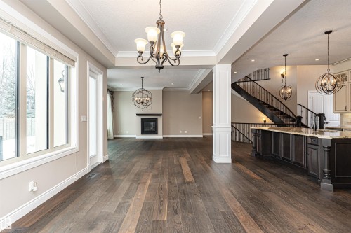 Unfurnished dining area with hanging lights, a glass covered fireplace, dark wood-style flooring, crown molding, and a textured ceiling - 3520 Watson Point(E), Edmonton, AB - Indoor With Fireplace