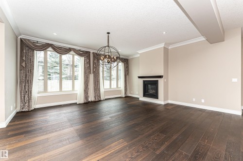 Unfurnished living room with hanging lights, dark wood-style floors, a glass covered fireplace, a textured ceiling, and ornamental molding - 3520 Watson Point(E), Edmonton, AB - Indoor Photo Showing Living Room With Fireplace