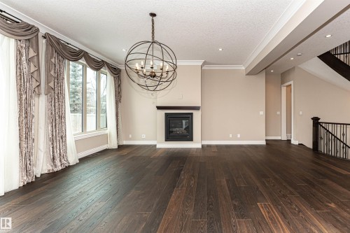 Unfurnished living room featuring ornamental molding, a glass covered fireplace, dark wood-style floors, a textured ceiling, and suspended lighting - 3520 Watson Point(E), Edmonton, AB - Indoor With Fireplace