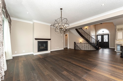 Unfurnished living room featuring a textured ceiling, dark wood finished floors, beverage cooler, a glass covered fireplace, and crown molding - 3520 Watson Point(E), Edmonton, AB - Indoor Photo Showing Living Room With Fireplace