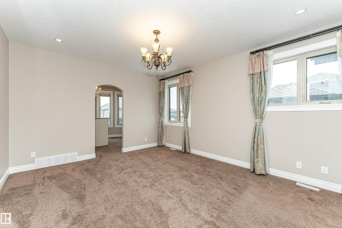 Carpeted spare room featuring healthy amount of natural light, a textured ceiling, a chandelier, and arched walkways - 3520 Watson Point(E), Edmonton, AB - Indoor Photo Showing Other Room