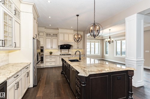 Dual tone kitchen with glass insert cabinets, light stone countertops, two tone cabinetry, tasteful backsplash, and a center island with sink - 3520 Watson Point(E), Edmonton, AB - Indoor Photo Showing Kitchen With Upgraded Kitchen