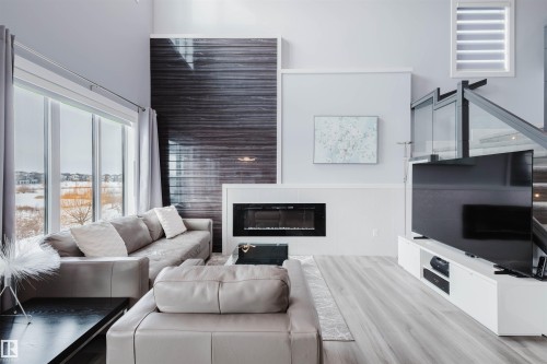 Living area with a glass covered fireplace, light wood finished floors, and a high ceiling - 16217 32 Avenue, Edmonton, AB - Indoor Photo Showing Living Room With Fireplace