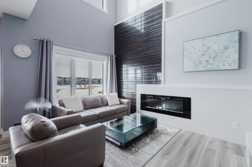 Living room with healthy amount of natural light, a glass covered fireplace, a high ceiling, and wood finished floors - 16217 32 Avenue, Edmonton, AB - Indoor Photo Showing Living Room With Fireplace