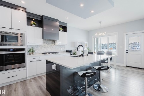 Dual tone kitchen featuring a kitchen bar, stainless steel appliances, modern cabinets, dual tone cabinetry, and a center island with sink - 16217 32 Avenue, Edmonton, AB - Indoor Photo Showing Kitchen With Upgraded Kitchen