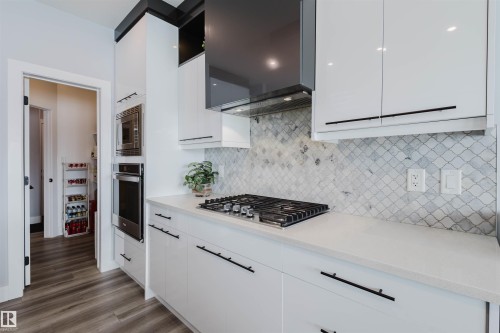 Kitchen with ventilation hood, stainless steel appliances, white cabinets, light wood finished floors, and modern cabinets - 16217 32 Avenue, Edmonton, AB - Indoor Photo Showing Kitchen With Upgraded Kitchen