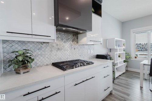 Kitchen featuring white cabinetry, open shelves, stainless steel gas stovetop, exhaust hood, and light stone counters - 16217 32 Avenue, Edmonton, AB - Indoor Photo Showing Kitchen With Upgraded Kitchen