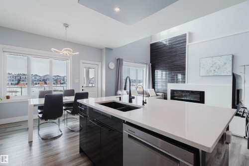 Kitchen featuring dark cabinetry, dark wood-style flooring, an island with sink, dishwasher, and open floor plan - 16217 32 Avenue, Edmonton, AB - Indoor Photo Showing Kitchen With Fireplace With Double Sink