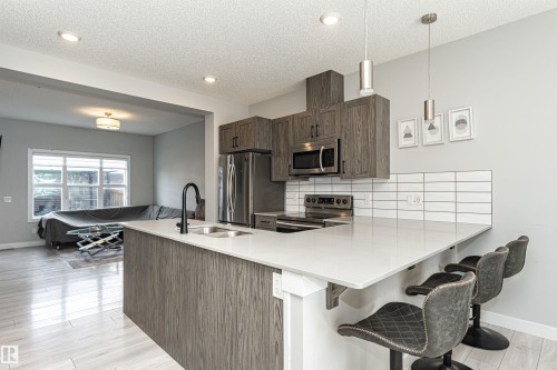 Kitchen with a peninsula, a breakfast bar area, stainless steel appliances, backsplash, and light stone counters - 16616 31 Avenue, Edmonton, AB - Indoor Photo Showing Kitchen With Double Sink With Upgraded Kitchen