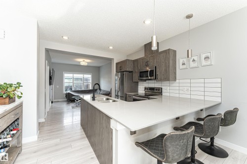 Kitchen with a breakfast bar, a peninsula, stainless steel appliances, light wood-type flooring, and a textured ceiling - 16616 31 Avenue, Edmonton, AB - Indoor Photo Showing Kitchen With Double Sink With Upgraded Kitchen