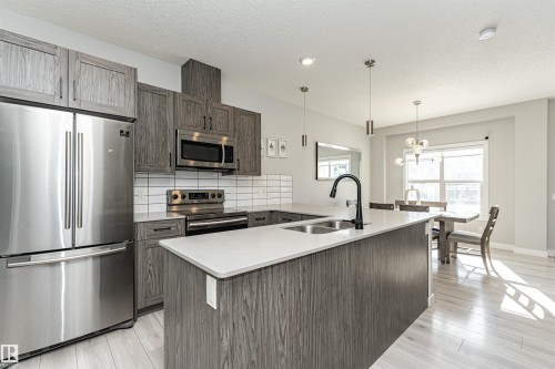 Kitchen with stainless steel appliances, a peninsula, hanging lights, light wood-style floors, and decorative backsplash - 16616 31 Avenue, Edmonton, AB - Indoor Photo Showing Kitchen With Double Sink With Upgraded Kitchen