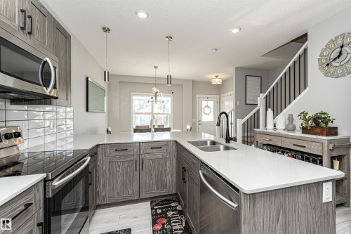 Kitchen featuring stainless steel appliances, a peninsula, pendant lighting, backsplash, and light wood-style flooring - 16616 31 Avenue, Edmonton, AB - Indoor Photo Showing Kitchen With Double Sink With Upgraded Kitchen