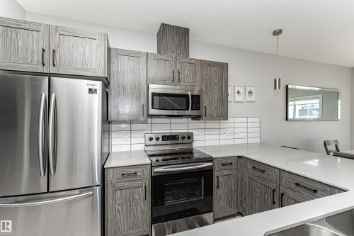 Kitchen with stainless steel appliances, decorative backsplash, decorative light fixtures, a peninsula, and a textured ceiling - 16616 31 Avenue, Edmonton, AB - Indoor Photo Showing Kitchen With Upgraded Kitchen