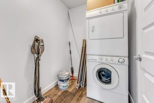 Laundry room with stacked washer and dryer and wood finished floors - 101 400 Silver Berry Road, Edmonton, AB - Indoor Photo Showing Laundry Room