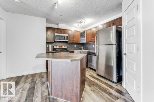 Kitchen featuring stainless steel appliances, tasteful backsplash, light countertops, rail lighting, and light wood-type flooring - 101 400 Silver Berry Road, Edmonton, AB - Indoor Photo Showing Kitchen