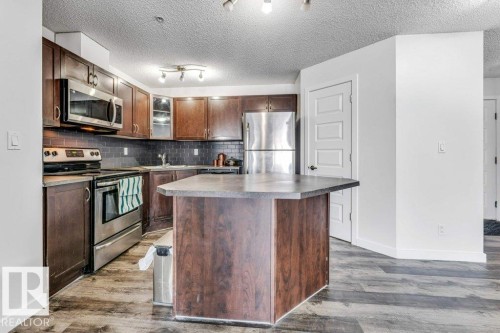 Kitchen featuring stainless steel appliances, a center island, dark wood-type flooring, backsplash, and glass insert cabinets - 101 400 Silver Berry Road, Edmonton, AB - Indoor Photo Showing Kitchen