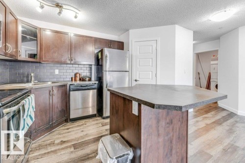 Kitchen featuring stainless steel appliances, glass insert cabinets, light wood-style flooring, a kitchen island, and tasteful backsplash - 101 400 Silver Berry Road, Edmonton, AB - Indoor Photo Showing Kitchen