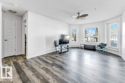 Living area featuring a ceiling fan, dark wood-style floors, and a textured ceiling - 101 400 Silver Berry Road, Edmonton, AB - Indoor Photo Showing Living Room