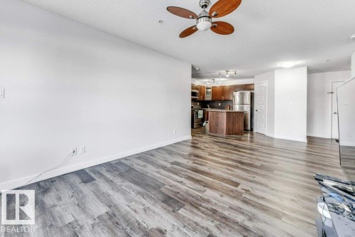 Unfurnished living room featuring a ceiling fan, dark wood-type flooring, and a textured ceiling - 101 400 Silver Berry Road, Edmonton, AB - Indoor
