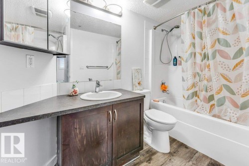 Full bathroom featuring vanity, shower / bathtub combination with curtain, light wood finished floors, and a textured ceiling - 101 400 Silver Berry Road, Edmonton, AB - Indoor Photo Showing Bathroom