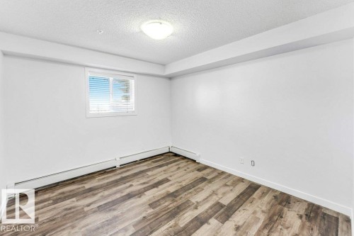 Unfurnished room with a textured ceiling, baseboard heating, and wood finished floors - 101 400 Silver Berry Road, Edmonton, AB - Indoor Photo Showing Other Room