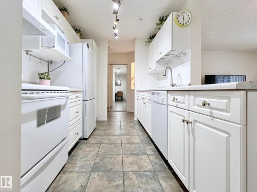 Kitchen with white cabinets, white appliances, light countertops, and a textured ceiling - 110 10511 42 Avenue, Edmonton, AB - Indoor Photo Showing Kitchen