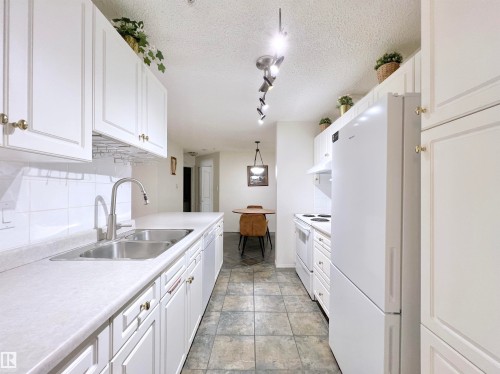 Kitchen featuring white appliances, white cabinets, a textured ceiling, light countertops, and decorative backsplash - 110 10511 42 Avenue, Edmonton, AB - Indoor Photo Showing Kitchen With Double Sink
