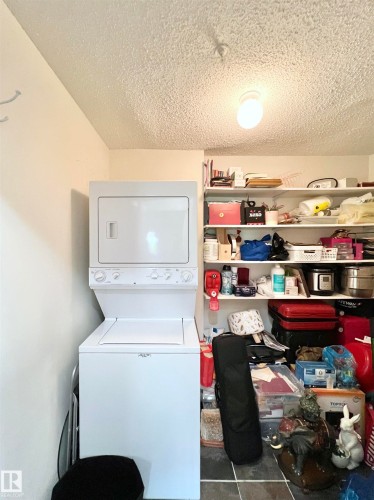 Laundry area with stacked washer / drying machine, a textured ceiling, and tile patterned floors - 110 10511 42 Avenue, Edmonton, AB - Indoor Photo Showing Laundry Room