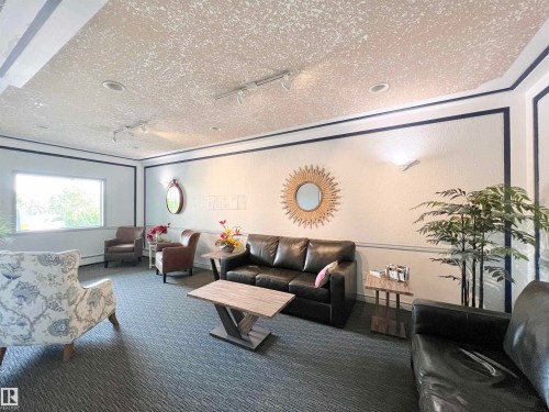 Carpeted living room with rail lighting, a textured ceiling, a textured wall, and a baseboard heating unit - 110 10511 42 Avenue, Edmonton, AB - Indoor Photo Showing Living Room