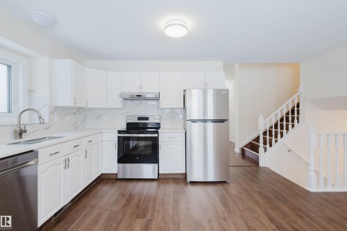 Kitchen featuring stainless steel appliances, white cabinetry, dark wood-type flooring, decorative backsplash, and light stone counters - 243 Rhatigan Road E, Edmonton, AB - Indoor Photo Showing Kitchen With Stainless Steel Kitchen
